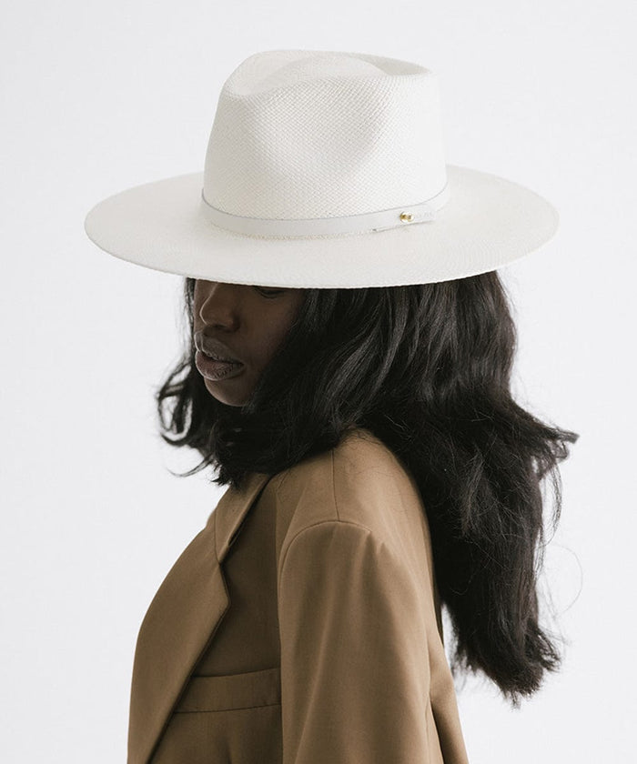 Woman wearing a white straw hat with a hat band and a brown coat, facing sideways against a plain background #color_white