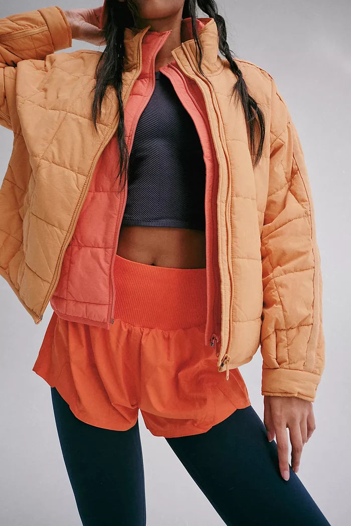 A model wearing high-waisted electric sunset shorts with built-in briefs and a knit waistband, paired with jackets and tank top
