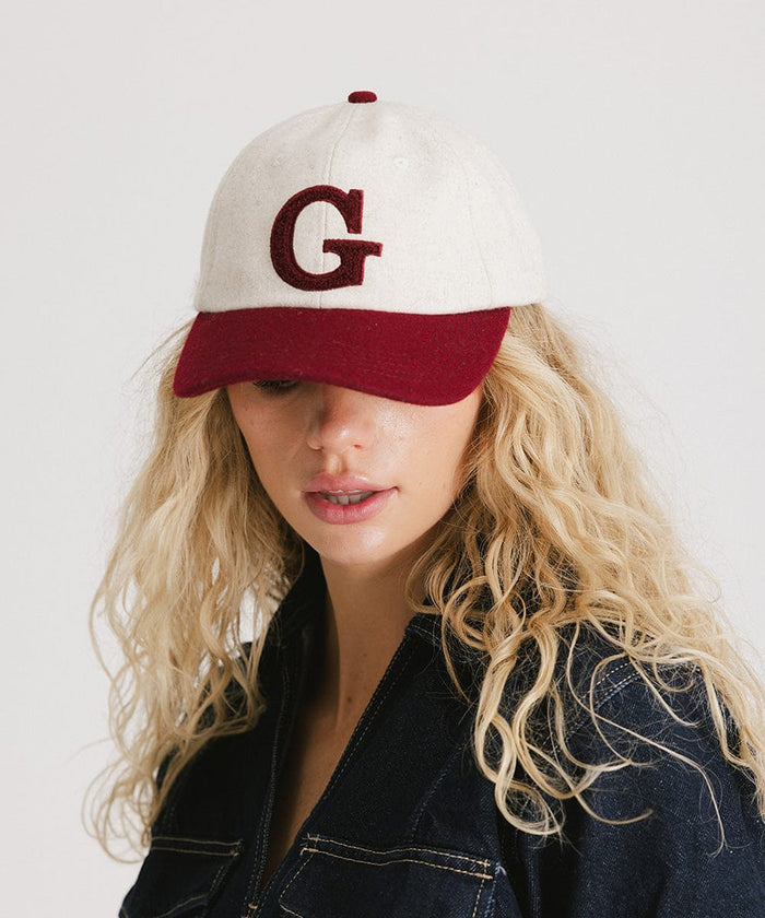 Woman wearing a white and burgundy baseball cap with the letter 'G' and a denim shirt, posing against a plain background  #color_burgundy