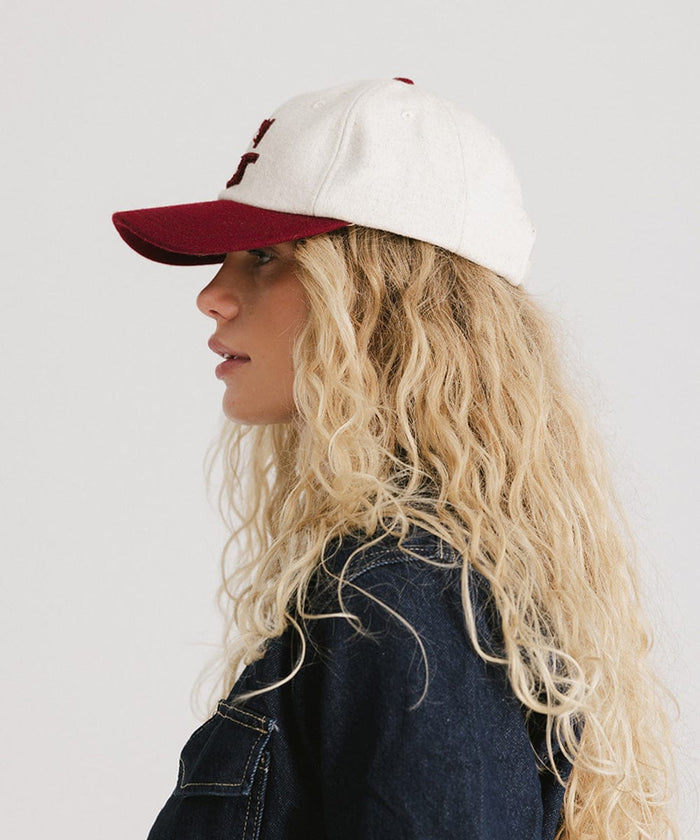 Woman wearing a white and burgundy baseball cap and a denim shirt, facing sideways against a plain background  #color_burgundy