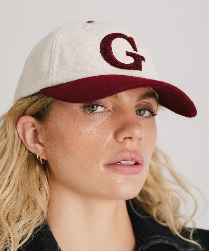 Woman wearing a white and burgundy baseball cap with the letter 'G' against a plain background  #color_burgundy
