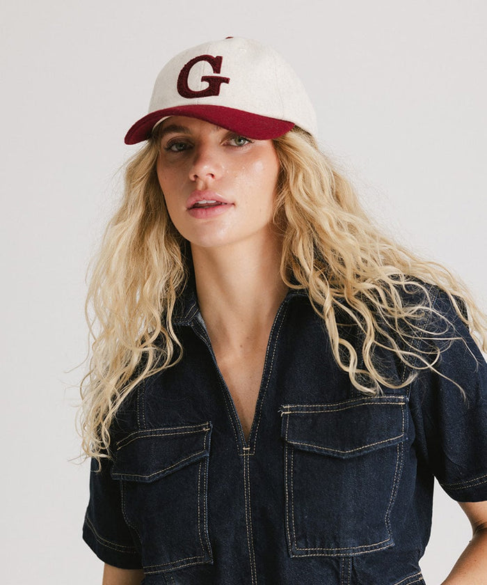 Woman wearing a white and burgundy baseball cap with the letter 'G' and a denim shirt against a plain background  #color_burgundy