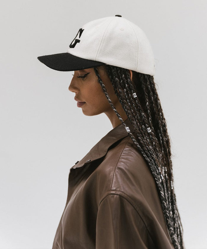 Woman wearing a cream and black baseball cap and a brown jacket, facing sideways against a plain background  #color_cream-black