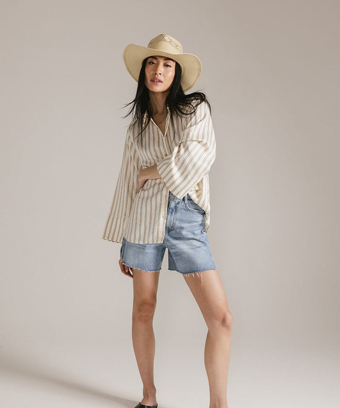 Woman wearing a striped shirt, denim shorts, and a hat against a plain background #color_natural
