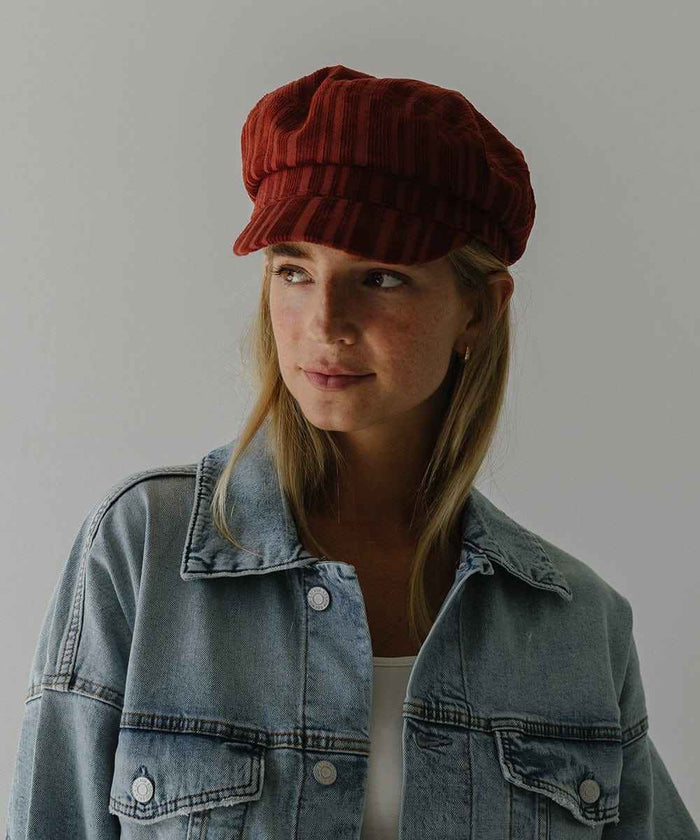 Woman wearing a crimson red colored striped cap and a denim shirt against a plain background #color_crimson red