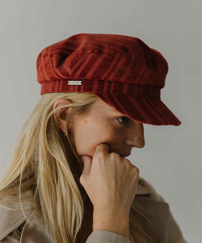 Woman wearing a crimson red colored striped cap posing sideways  against a plain background #color_crimson red