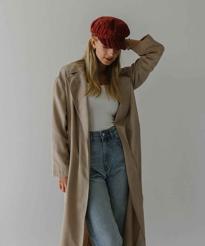 Woman wearing a crimson red colored striped cap, a white top with a beige jacket and blue jeans, posing  against a plain background #color_crimson red