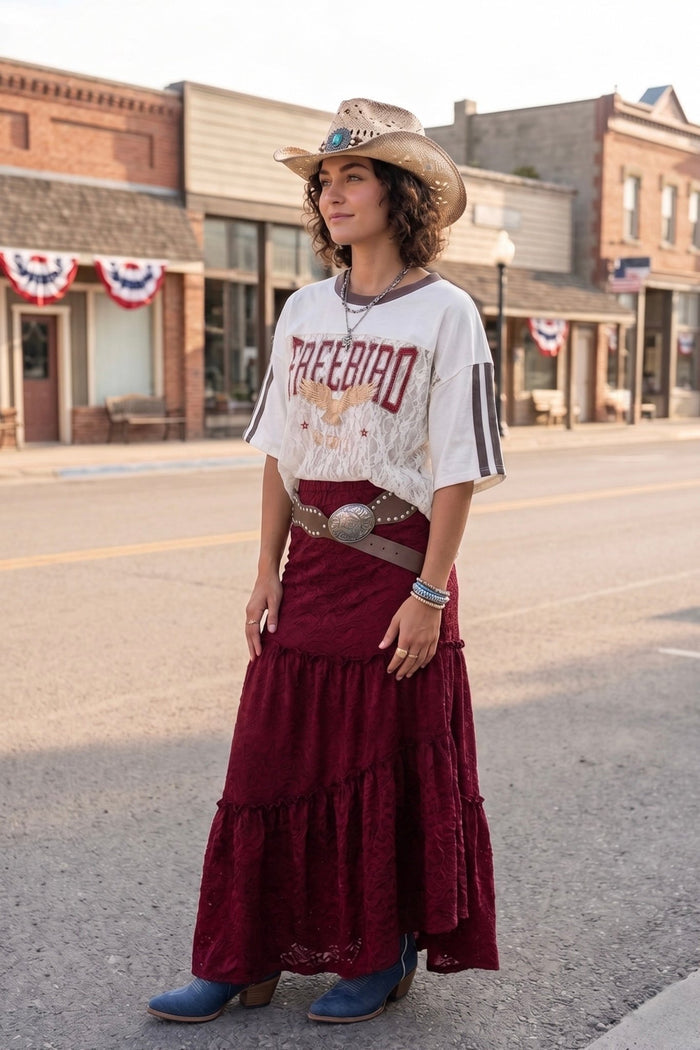 Free Bird graphic tee featuring lace overlay details and contrast stripe sleeves, styled with a western hat and lace skirt for a country concert outfit, rodeo fashion, festival wear, and boho western boutique style.