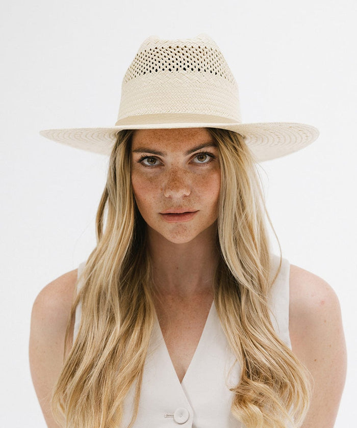 Woman wearing a natural colored straw cowboy hat and a white top against a plain background  #color_natural