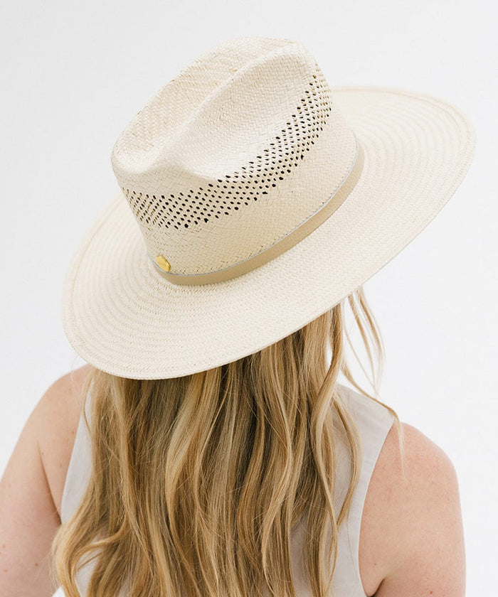 Person wearing a natural colored straw cowboy hat with a hat band and a white top against a plain background  #color_natural