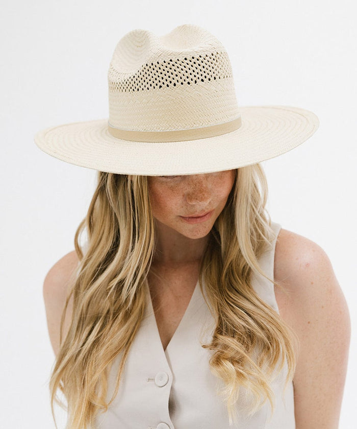 Woman wearing a natural colored straw cowboy hat with a hat band  and a white top against a plain background  #color_natural