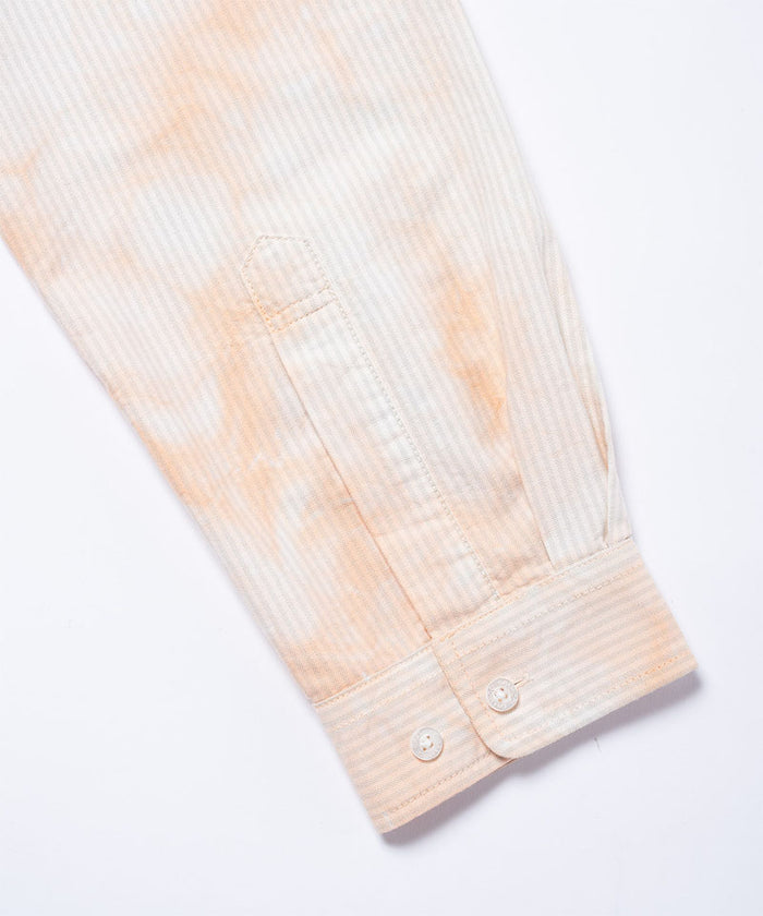 Close-up of the cuff and sleeve on a peach Bleach Stripe colored Gramicci Classic Oxford Bleached Shirt on a light-tone background.
