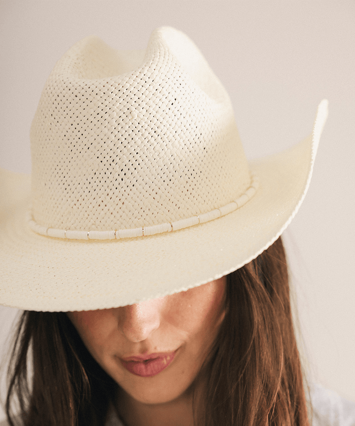 Woman wearing a beige straw hat with a decorative band in a white background #color_cream