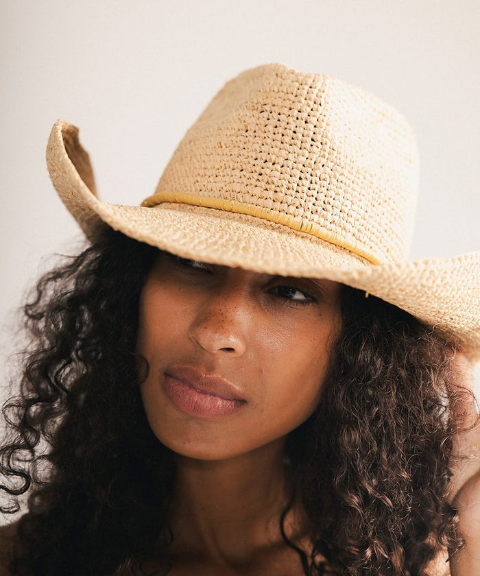 Woman wearing a straw hat with a decorative band against a plain background #color_tan