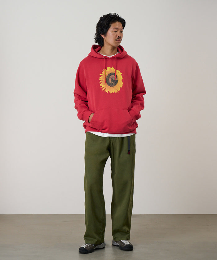 Model wearing olive Gramicci Cliff Pants and a red hoodie on a light-tone background.