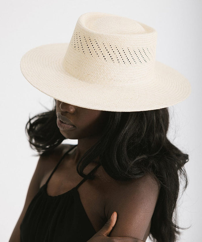 Woman wearing a natural colored straw hat and a black top, posing sideways against a plain background #color_natural