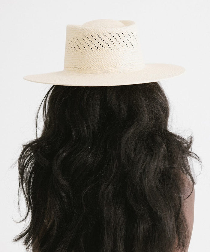 Woman with long hair wearing a natural colored straw hat against a plain background #color_natural