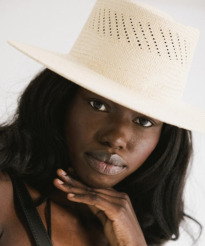 Close up image of a woman wearing a natural colored straw hat against a plain background #color_natural