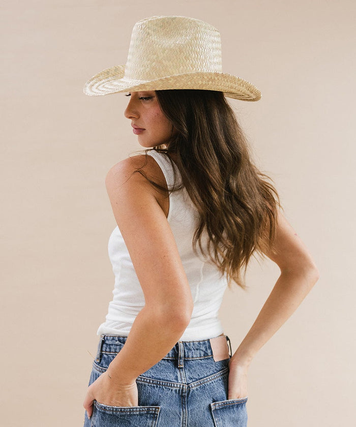 Woman wearing a natural colored straw cowboy hat, a white top and blue jeans, looking sideways against a plain background  #color_natural