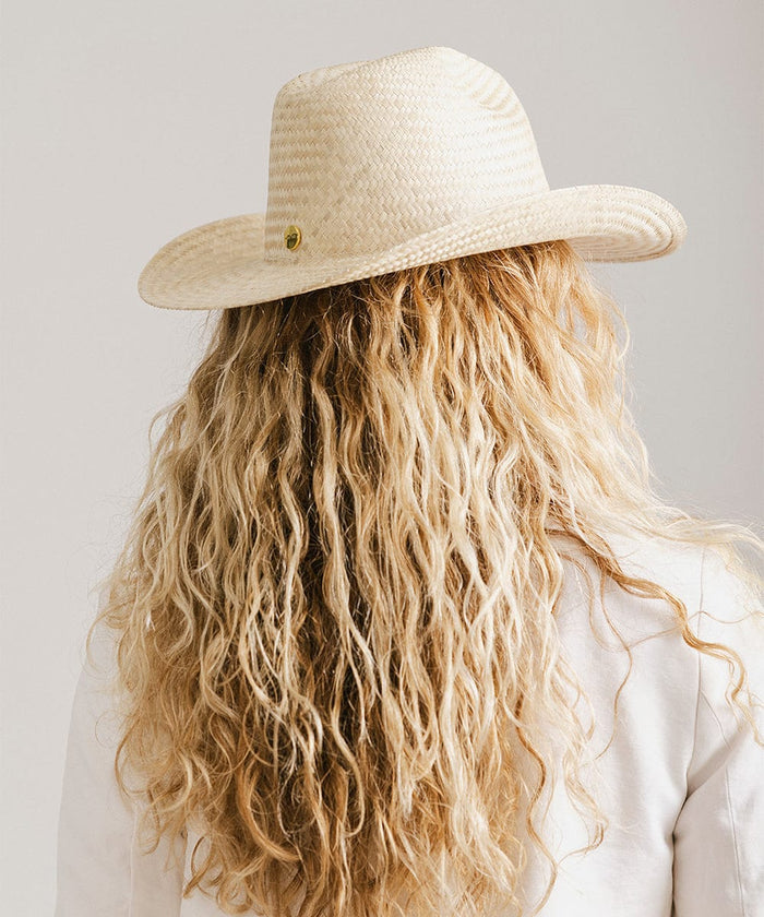 Woman with long blonde hair wearing a natural colored straw cowboy hat and a white jacket against a plain background  #color_natural