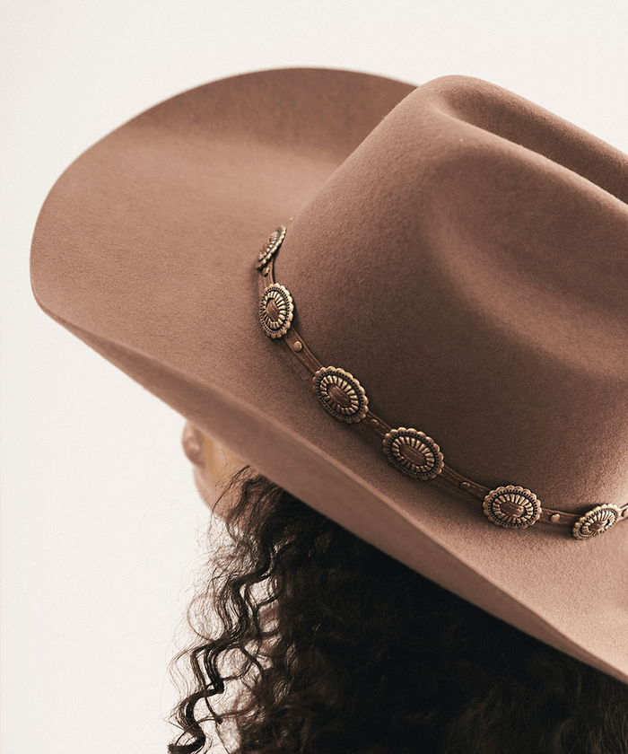 Woman wearing a brown cowboy hat with decorative band against a neutral background #color_chocolate