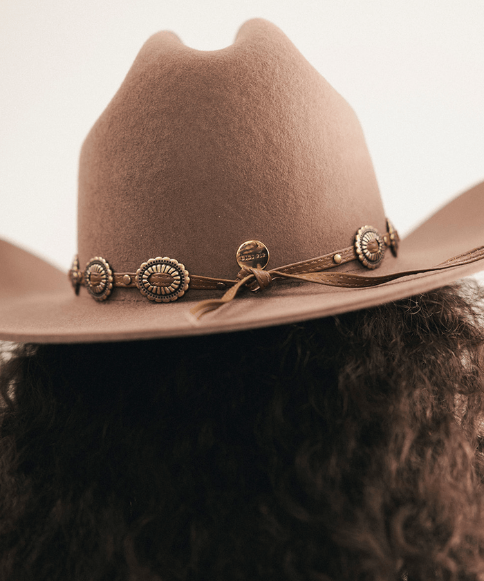Woman wearing a brown cowboy hat with decorative band against a neutral background #color_chocolate