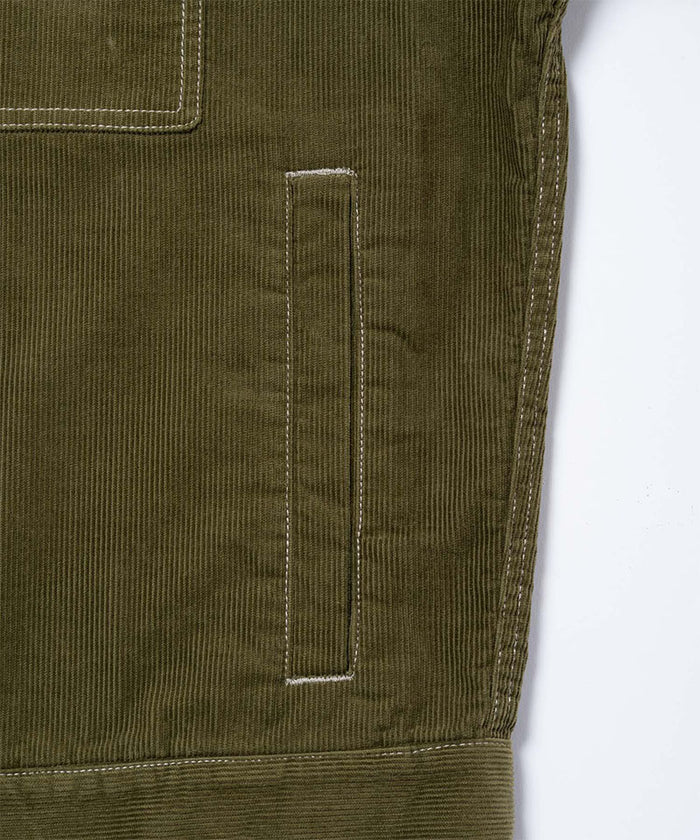 Close-up of a olive Gramicci Corduroy Trucker Jacket on a light-tone background.