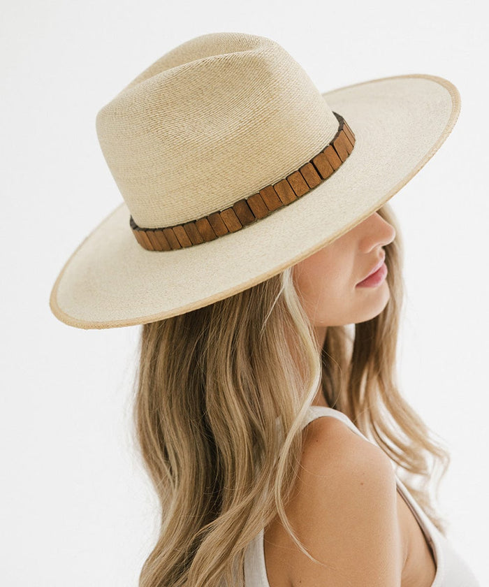 Woman wearing a natural colored wide brim straw hat with a hat band, facing sideways against a plain background  #color_natural
