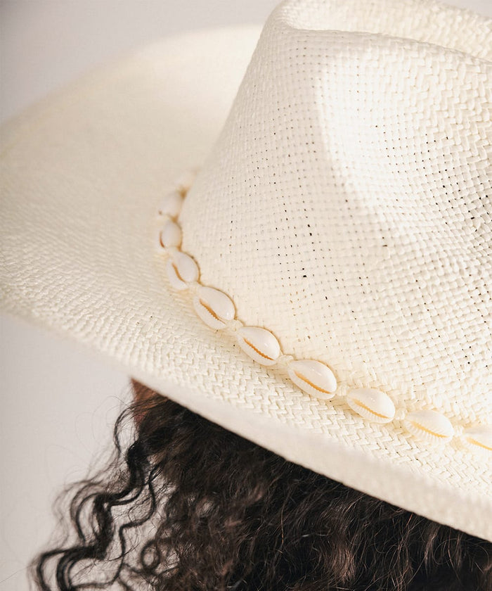 Close-up of a person wearing a white straw hat with shell embellishments #color_natural