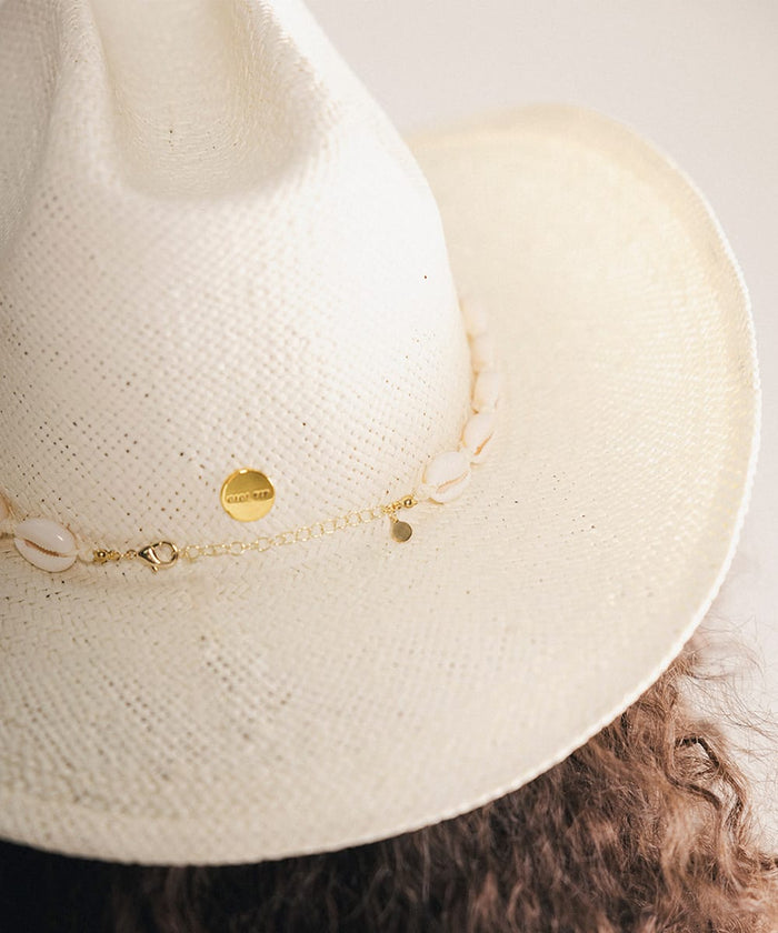 Close-up of a woman wearing a white straw hat with shell embellishments and gold Gigi Pip pin #color_natural