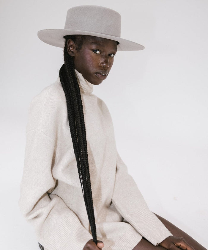 Woman with long hair wearing a light grey boater-style hat and a cream sweatshirt against a plain background #color_light grey