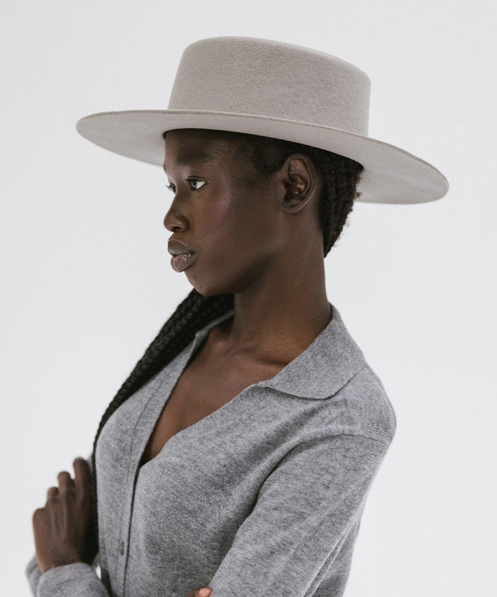 Woman wearing a light grey boater-style hat and a grey shirt, facing sideways against a plain background #color_light grey