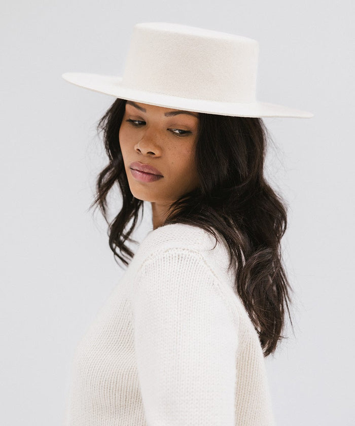 Woman wearing an off white boater-style hat and a white sweatshirt, posing against a plain background #color_off white