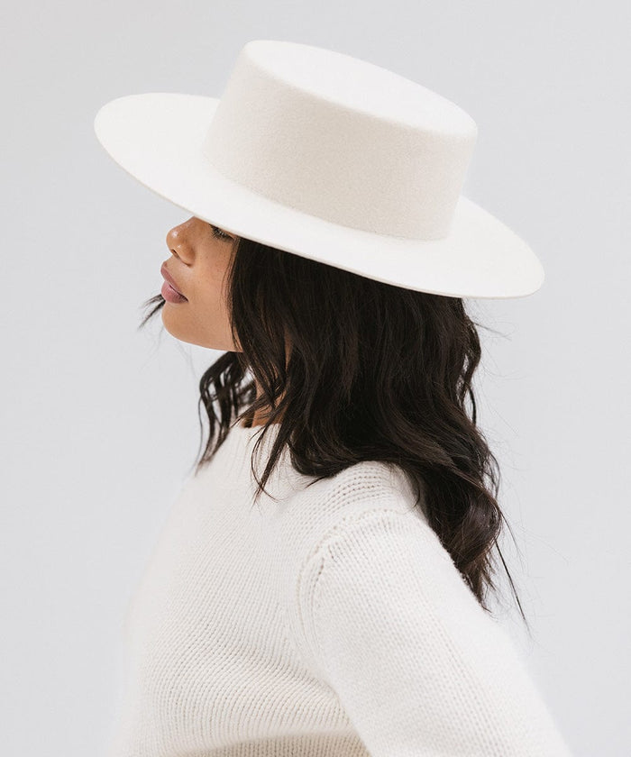 Woman wearing an off white boater-style hat and a white sweatshirt facing sideways against a plain background #color_off white