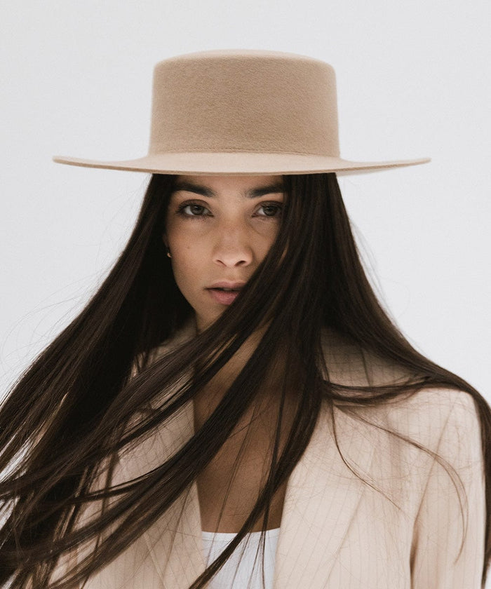 Woman with long hair wearing a tan boater-style hat and a cream blazer against a plain background #color_tan
