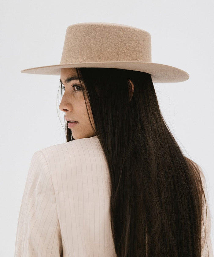 Woman with long hair wearing a tan boater-style hat and a cream blazer, posing against a plain background #color_tan