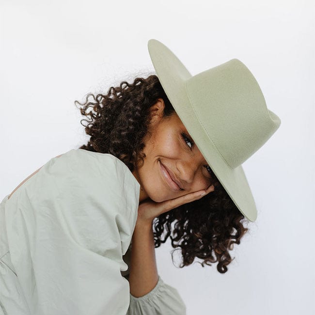 Woman wearing a light green fedora hat and a grey top, posing against a plain background #color_light green