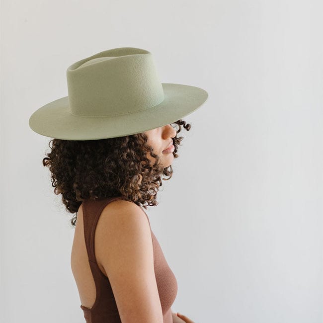 Woman wearing a light green fedora hat and a brown top, facing sideways against a plain background #color_light green
