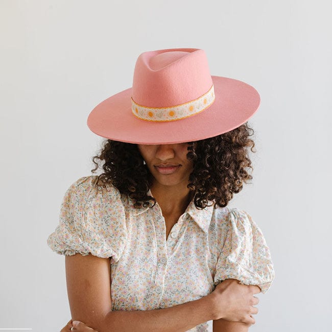 Woman wearing a pink Dakota Dae Triangle Crown hat with a band and a light colored top, looking down  against a plain background #color_pink