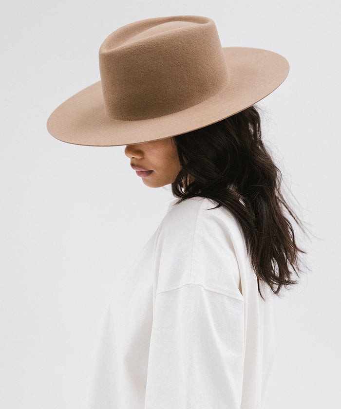 Woman wearing a brown wide brim felt hat with a triangle crown and a white shirt, facing sideways against a white background #color_brown
