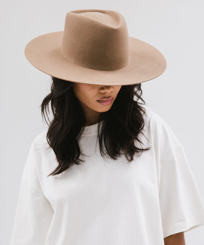 Woman wearing a brown wide brim felt hat with a triangle crown and a white shirt, looking down against a white background #color_brown