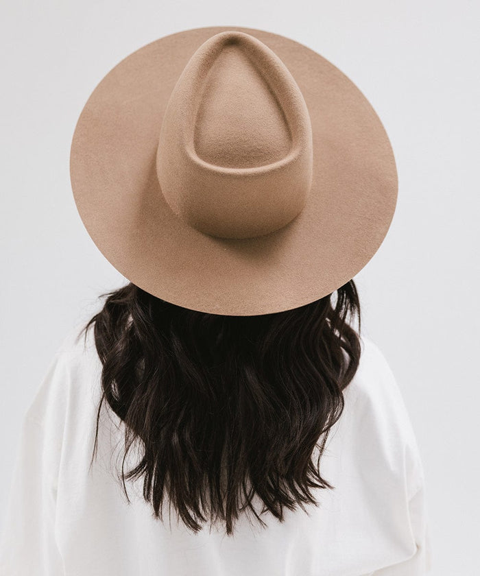 Woman wearing a brown wide brim felt hat with a triangle crown and a white shirt, facing behind against a white background #color_brown