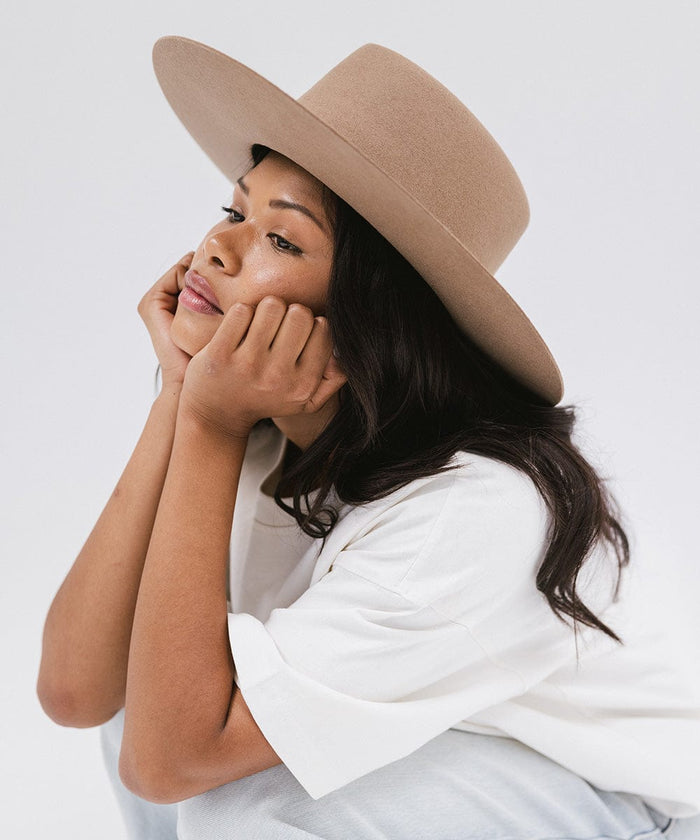 Woman wearing a brown wide brim felt hat with a triangle crown and a white shirt, looking sideways against a white background #color_brown