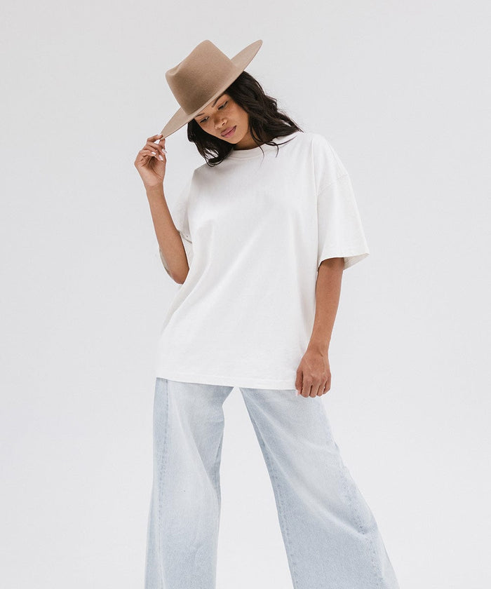 Woman wearing a brown wide brim felt hat with a triangle crown, a white shirt, and jeans against a white background #color_brown
