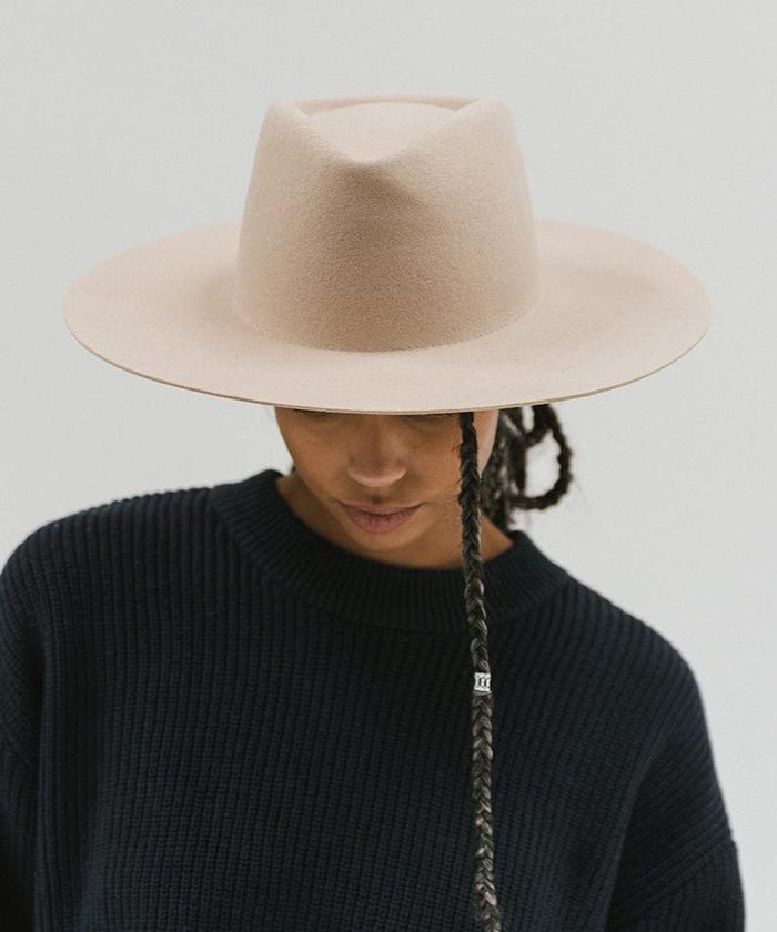Woman wearing a cream wide brim felt hat with a triangle crown and a dark blue sweatshirt against a white background #color_cream