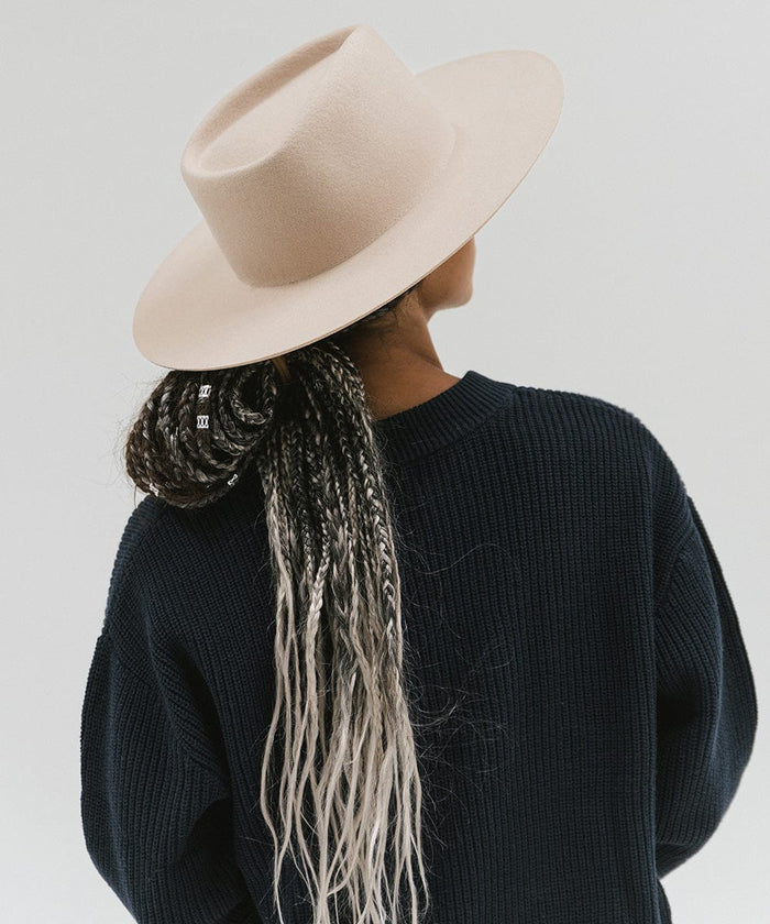 Woman wearing a cream wide brim felt hat with a triangle crown and a dark blue sweatshirt, facing behind against a white background #color_cream