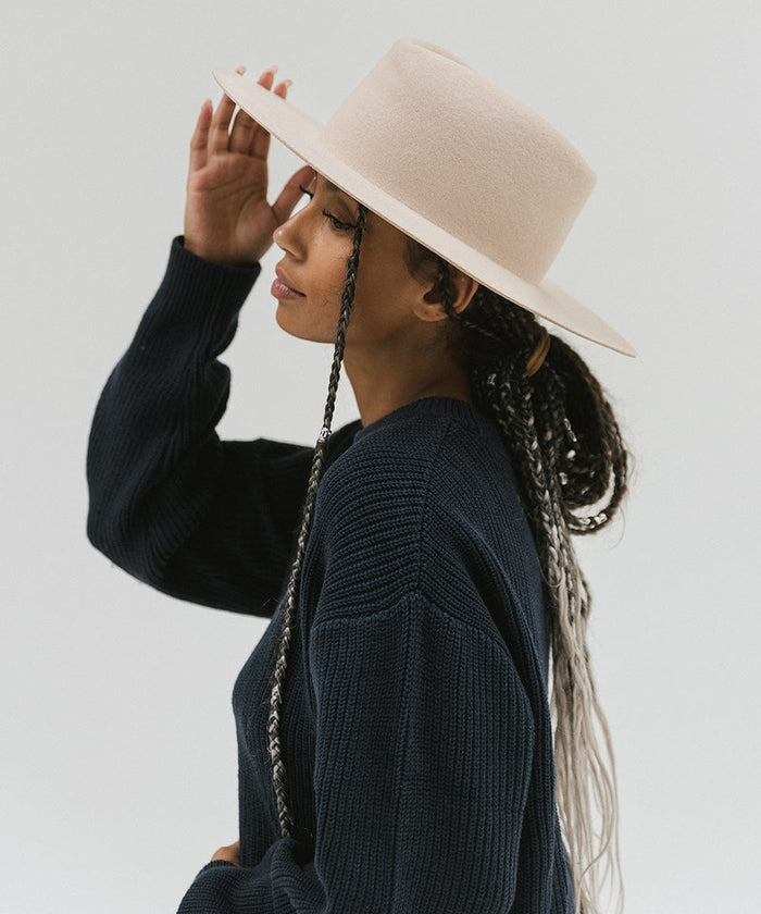 Woman wearing a cream wide brim felt hat with a triangle crown and a dark blue sweatshirt, looking sideways against a white background #color_cream