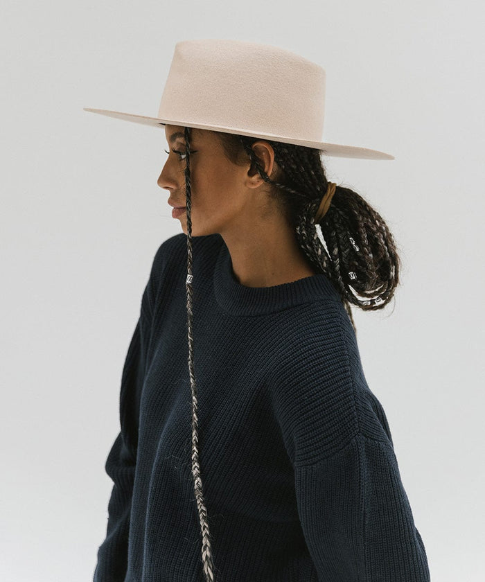 Woman wearing a cream wide brim felt hat with a triangle crown and a dark blue sweatshirt, facing sideways against a white background #color_cream