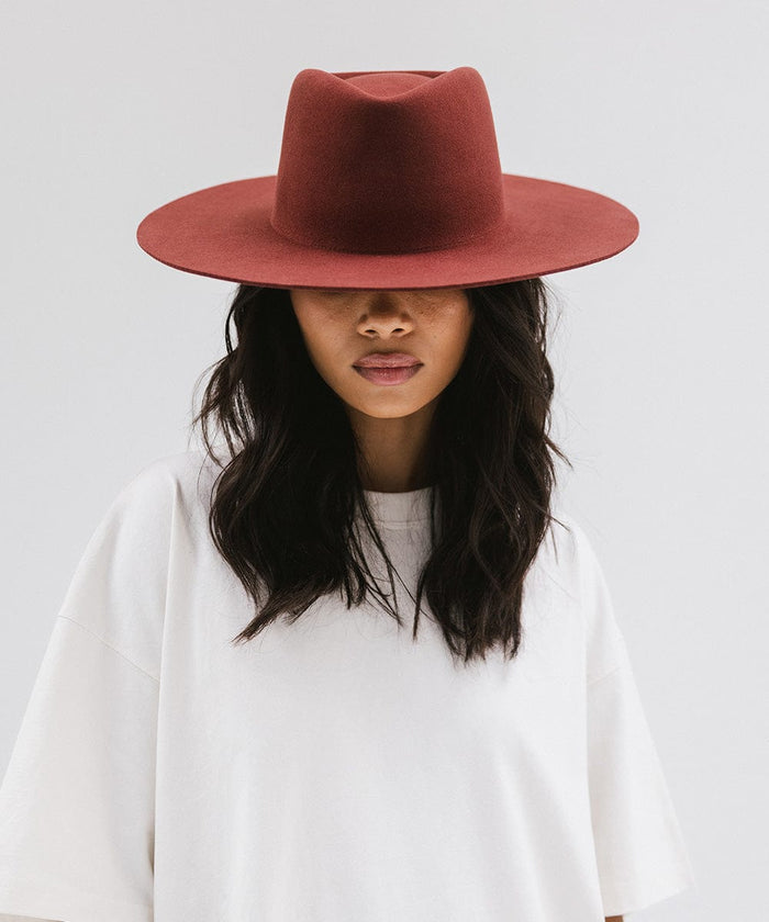 Woman wearing a rusty red wide brim felt hat with a triangle crown and a white t-shirt against a white background #color_rusty red