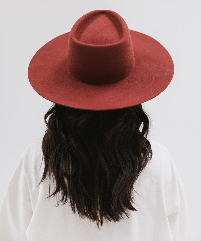 Woman wearing a rusty red wide brim felt hat with a triangle crown and a white t-shirt, facing behind against a white background #color_rusty red